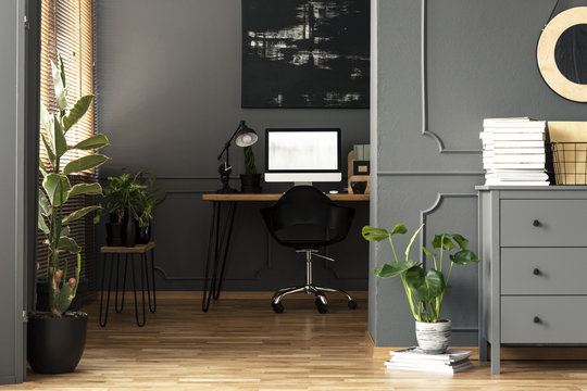 Black painting above desk with lamp and computer desktop in grey apartment interior. Real photo