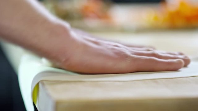 Close up hands of unrecognizable male cook shaping pizza crust on floured wooden surface in kitchen