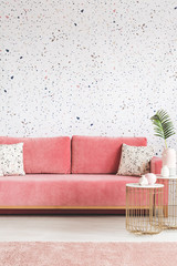 Gold table in front of pink settee with pillows in patterned living room interior with carpet. Real...