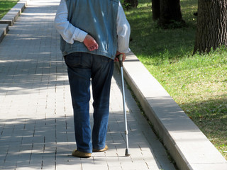 Elderly man walking with a cane in a summer park. Old age, pension or diseases of the spine concept
