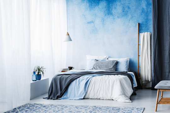 Grey and blue bedding on bed against ombre wall in minimal bedroom interior with ladder