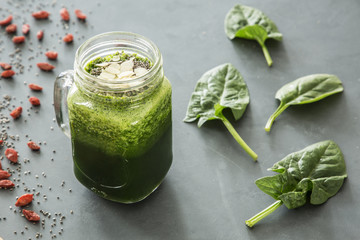 High angle on leaves of spinach next to green healthy cocktail on grey background