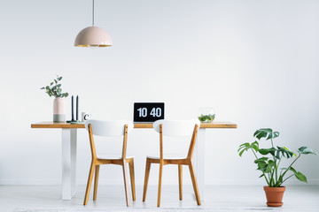 White chairs at wooden table with laptop in workspace interior with plant and pink lamp. Real photo