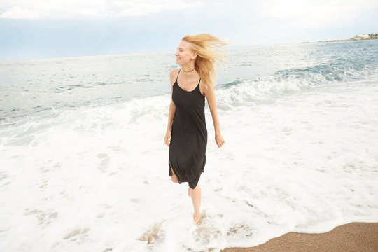 A blonde girl is stepping inside the Mediterranean sea enjoying the water, waves and drops in Barcelona