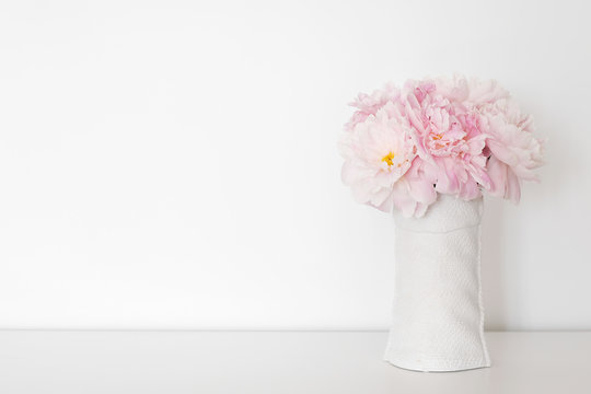 White wall of the room On the table is a conceptual vase with flowering pink peonies.