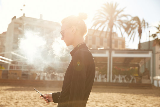 A girl smoking vape on Barceloneta beach in Barcelona