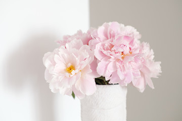 Angle of white and gray walls in room. On dresser stands white vase with pink flowers blooming peonies.