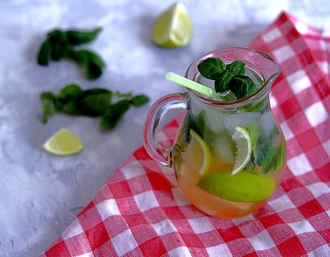 Cold summer drink, lemonade with lime and basil on the basis of sparkling water and sugar syrup in a small glass jug. Served with ice. Summer concept.