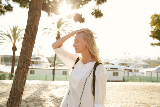 Portrait of a model blond girl walking around Barcelona coast with dock and yachts under the palms