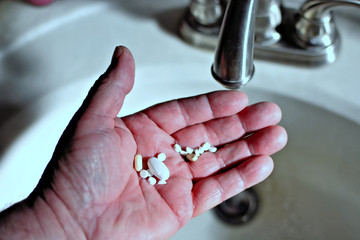 A closeup of a senior's hand ready to throw his pills down the drain