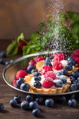  Dessert tarts with raspberries and blueberries on a wooden table.