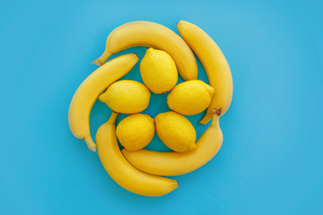yellow bananas and lemons in circle on bright blue paper, trendy flat lay. fruits modern image, top view. juicy summer vitamin abstract background. pop art style. creative minimalism.
