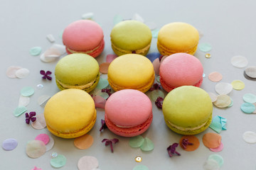 colorful macarons on trendy pastel gray paper with lilac flowers and confetti. tasty pink, yellow, green and brown macaroons. candy bar for party. food photography. yummy background