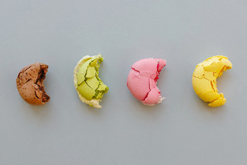 tasty bitten yellow, pink, green and brown macarons on trendy pastel gray paper, flat lay. space for text. delicious colorful macaroons candy for party. yummy background. diet concept