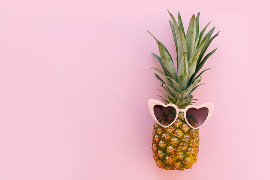 pineapple in pink sunglasses on trendy pink paper background. minimalism flat lay. summer vacation and party concept. space for text. hipster summer holidays