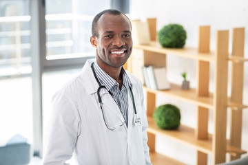 Cheerful dark-skinned practitioner keeping stethoscope