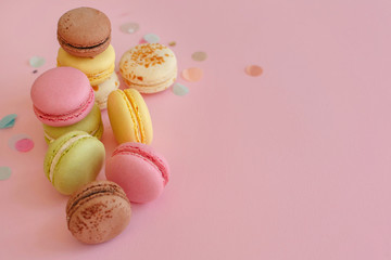 tasty colorful macarons on trendy pastel pink paper with confetti. space for text pink, yellow, green, white, brown macaroons. modern food photography concept. luxury catering