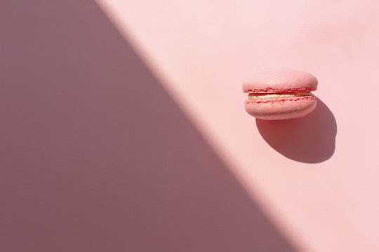tasty pink macaron in sunny light on trendy pastel pink paper flat lay. space for text. pink macaroon in light contrast. modern food photography concept. minimalism concept