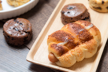 closeup delicious sausage bread roll and fresh tasty scones on wooden table