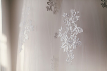 Fototapeta na wymiar beautiful floral detail on silk wedding dress. lace ornament on white gown, bridal morning preparations