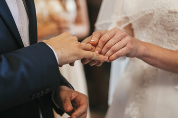 beautiful bride and groom hands exchanging wedding rings in church during wedding ceremony....