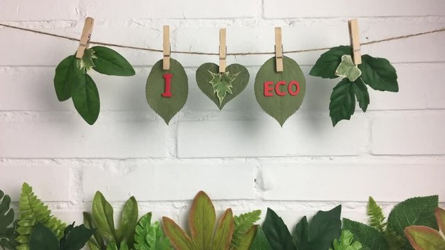 Frase &ldquo;I love eco&rdquo; en una cuerda con hojas sobre fondo de ladrillos.
