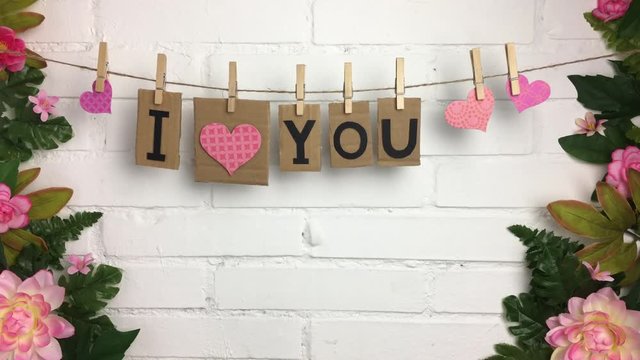 Frase &ldquo;I love you&rdquo; colgando de una cuerda con pinzas, rodeado de plantas y flores.