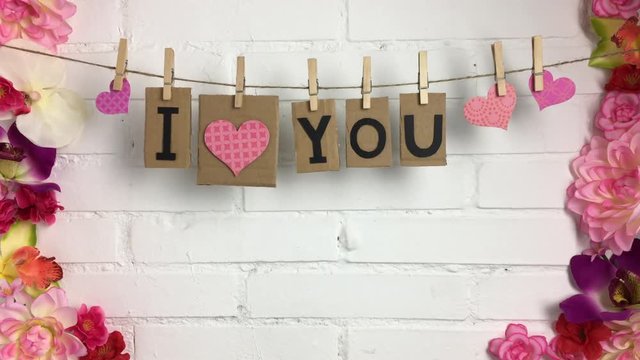 Frase &ldquo;I love you&rdquo; colgando de una cuerda con pinzas, rodeado de flores.