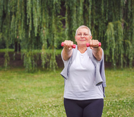 Mature woman with dumbbell exercise with dumbbells in a park .