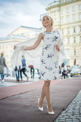 Full length of beautiful girl in dress holding scarf around shoulders and walking on red carpet outdoors.