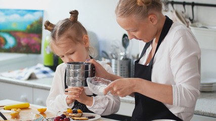 Woman with her child puts sugar in the pancakes