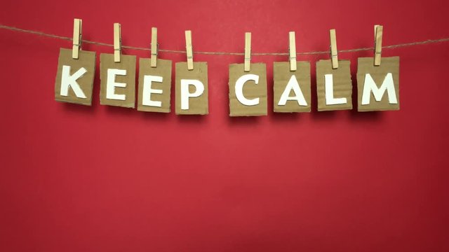 Frase &ldquo;keep calm&rdquo; colgando en una cuerda con pinzas sobre fondo rojo.
