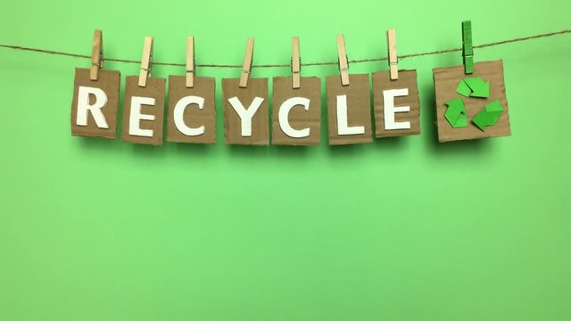 Word "recycle" hanging from a string with tweezers.