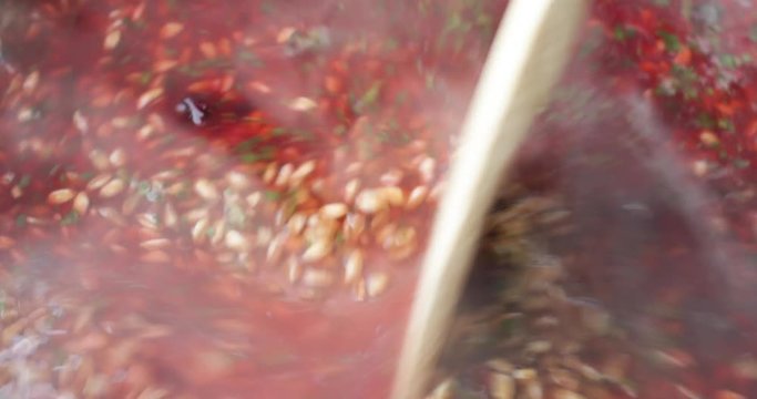Close video of stirring farro with beets and spinach and seasonings in boiling water with a wood spoon.