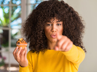 Fototapeta na wymiar African american woman holding chocolate muffin pointing with finger to the camera and to you, hand sign, positive and confident gesture from the front