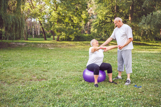 Concept of healthy lifestyle -Mature man and woman doing together fitness exercises on fitness ball in park . - Powered by Adobe