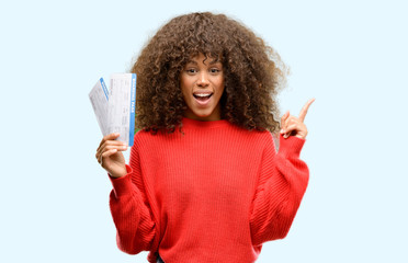 African american woman holding airline boarding pass tickets surprised with an idea or question pointing finger with happy face, number one