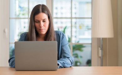 Young woman using laptop at home with a confident expression on smart face thinking serious