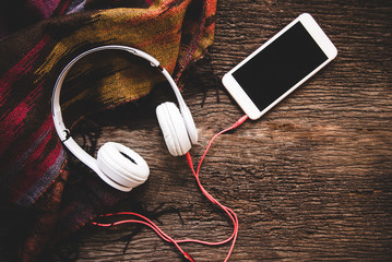 Cozy winter background, cup of hot coffee with marshmallow and headphone music, warm knitted sweater, vintage tone. Lifestyle and music concept.