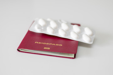 Deutscher Reisepass mit daraufliegender weißen Tablettenpackung als Reiseapotheke auf weißem...