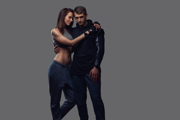 Attractive couple, slim brunette female and handsome guy in sportswear cuddling in a studio on a dark textured background.