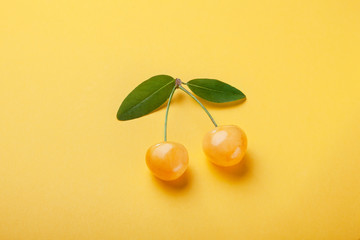 Two yellow cherries with green leaf on  yellow background, good postcard.