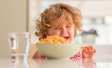 Beautiful blond child eating spaghetti with hands crying with tantrum at home.