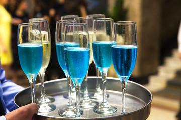 The waiters greet guests with alcoholic drinks. Champagne, blue wine, white wine on trays.