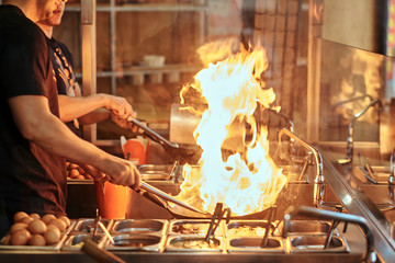 Cooking process in an Asian restaurant. Cook is fry vegetables with spices and sauce in a wok on a...