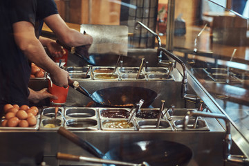 Cooking process in an Asian restaurant. Cook is stirring vegetables in wok.