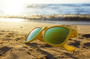 Yellow sunglasses in the sand on the beach closeup. sun and sea waves in background, depth of field...