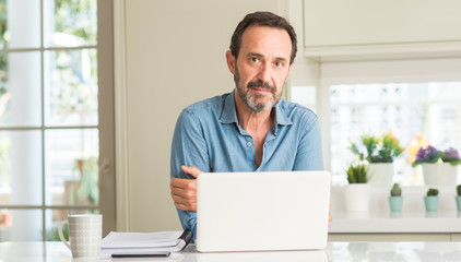 Middle age man using laptop at home with a confident expression on smart face thinking serious