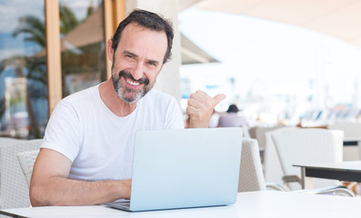 Fototapeta premium Handsome senior man using laptop at restaurant pointing with hand and finger up with happy face smiling