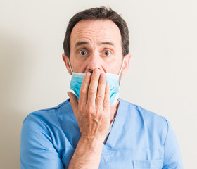 Senior doctor man using mask cover mouth with hand shocked with shame for mistake, expression of...